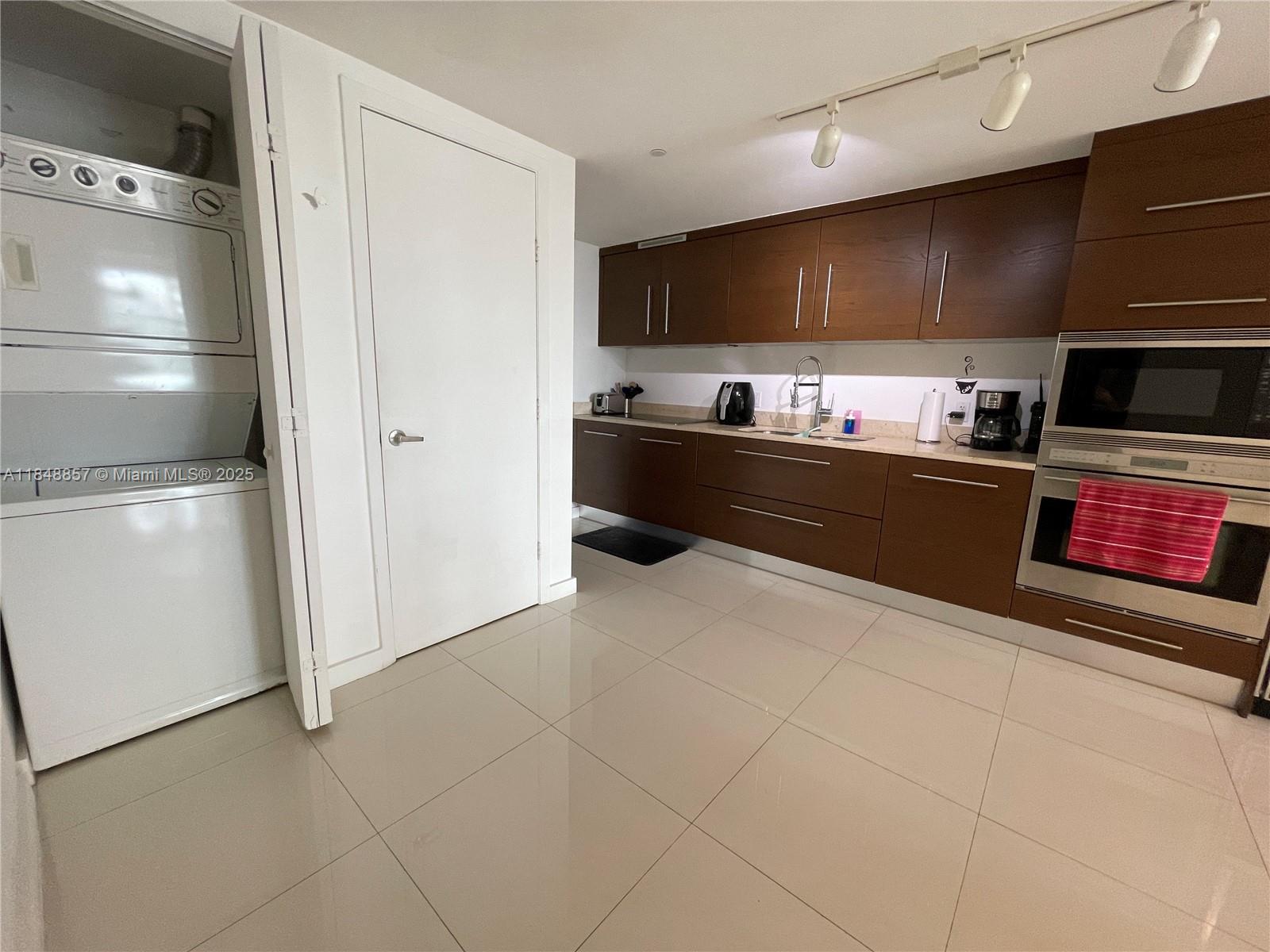 A kitchen features dark wood cabinets, stainless steel appliances, and a stacked laundry unit — 485 Brickell Ave # 3711, Miami FL 33131, MIAMI, FL