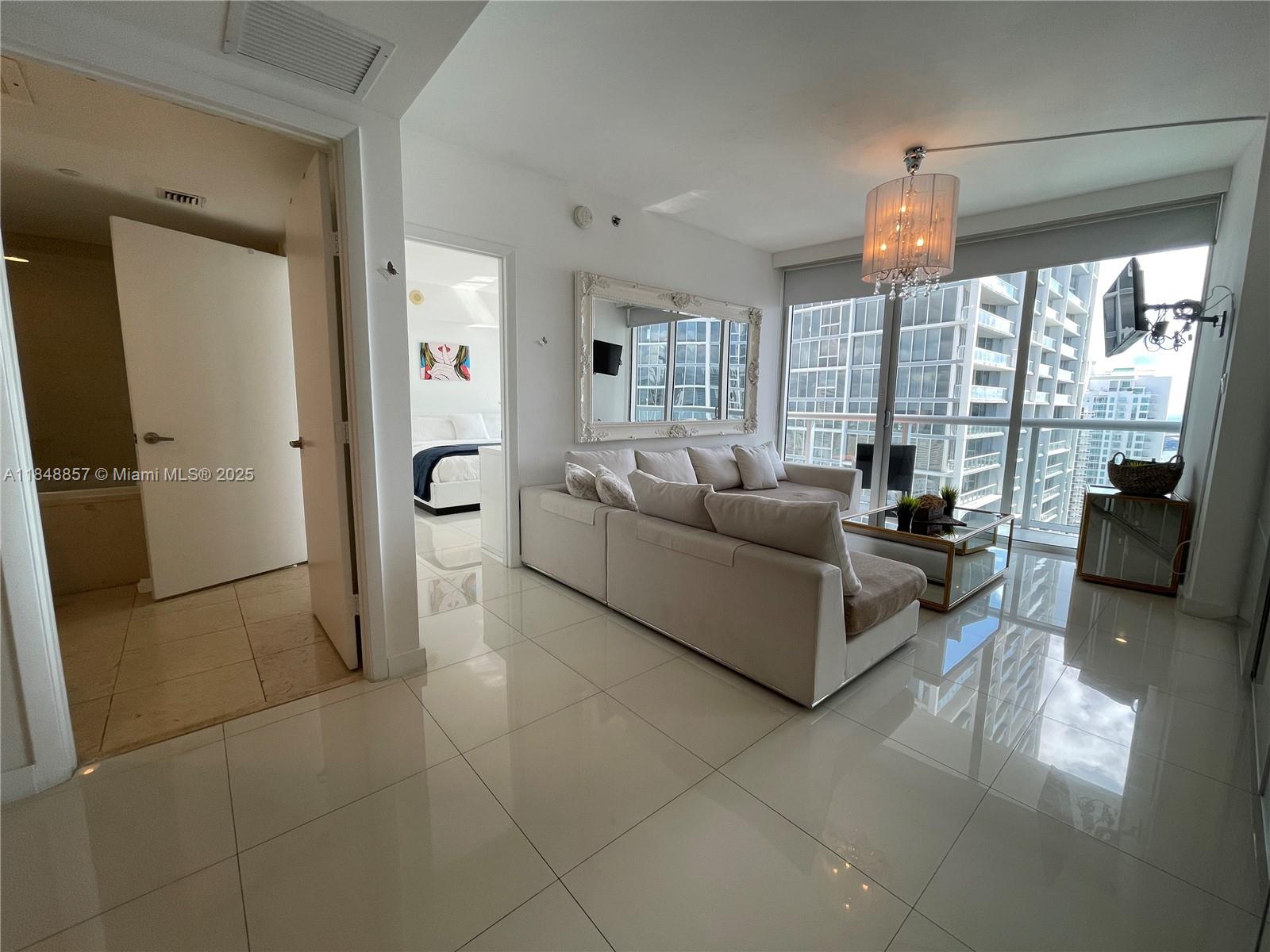 A living room with white tile floors, a sectional sofa, and floor-to-ceiling windows — 485 Brickell Ave # 3711, Miami FL 33131, MIAMI, FL