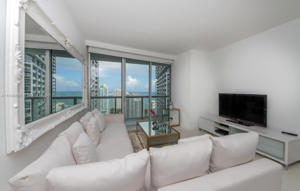A living room features a white sectional sofa, a mirrored coffee table, and floor-to-ceiling windows — 485 Brickell Ave # 3711, Miami FL 33131, MIAMI, FL