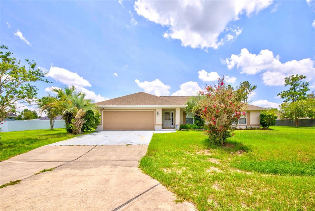 A single-story house with a tan garage, concrete driveway, and a front yard with trees — 4818 SW 114TH STREET, OCALA, FL