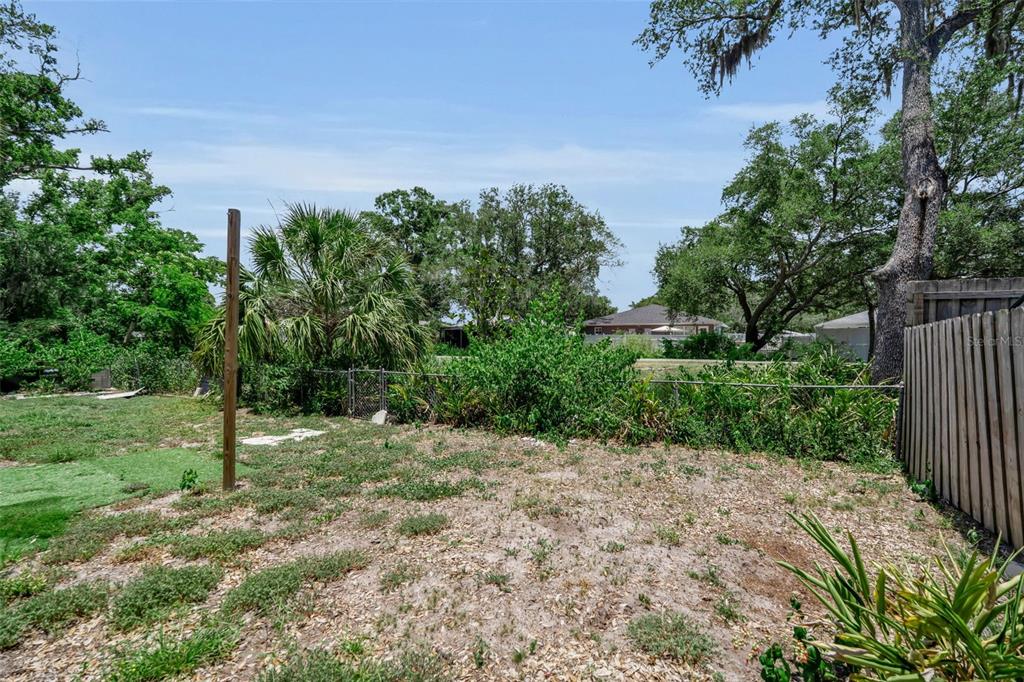 A grassy backyard features a wooden fence, a chain-link fence, and mature trees — 2223 INGRAM AVENUE, SARASOTA, FL