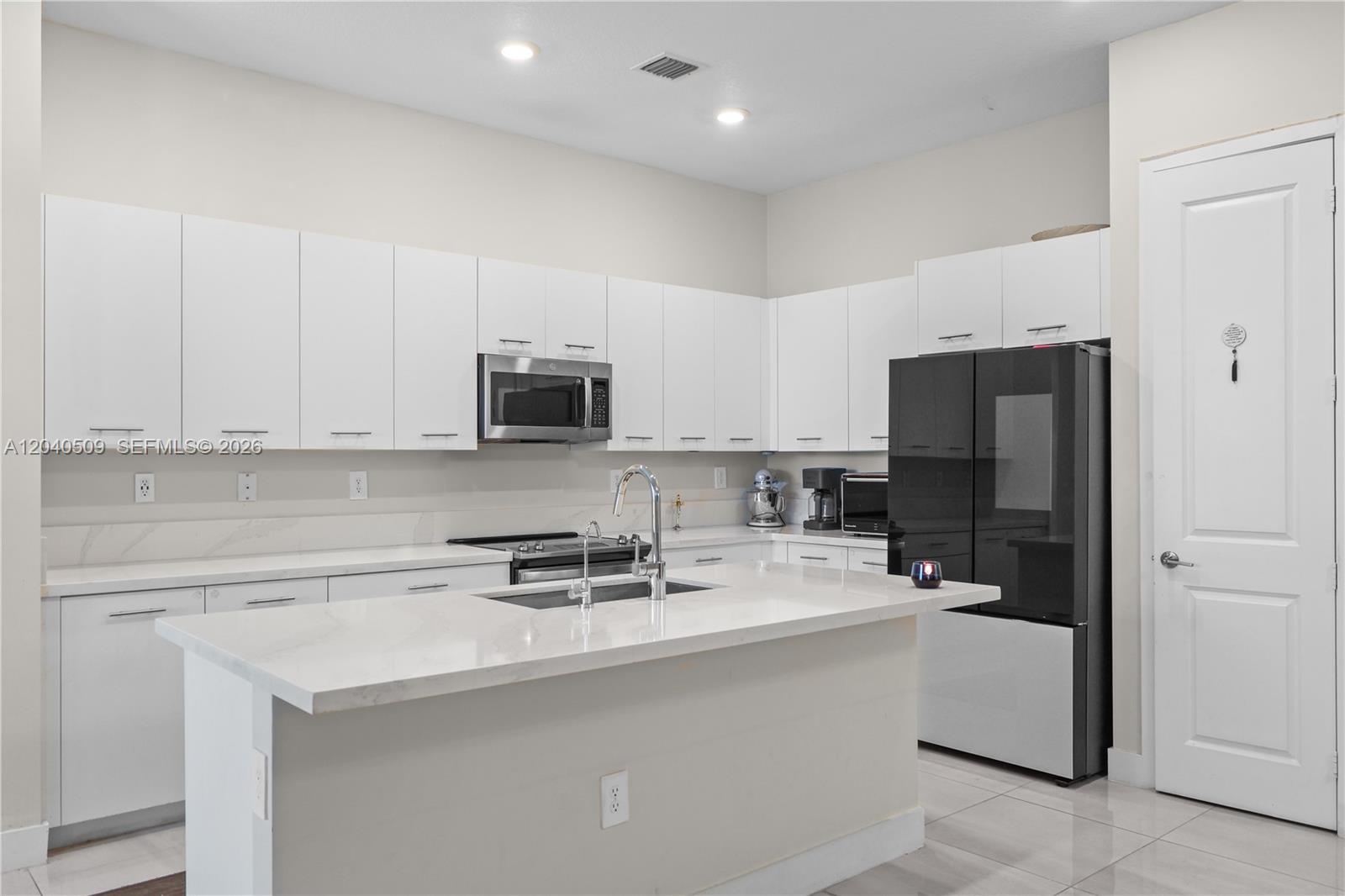 A modern kitchen features white cabinets, a central island with a sink, and black appliances — 17384 SW 41st St, Miramar FL 33029, MIRAMAR, FL