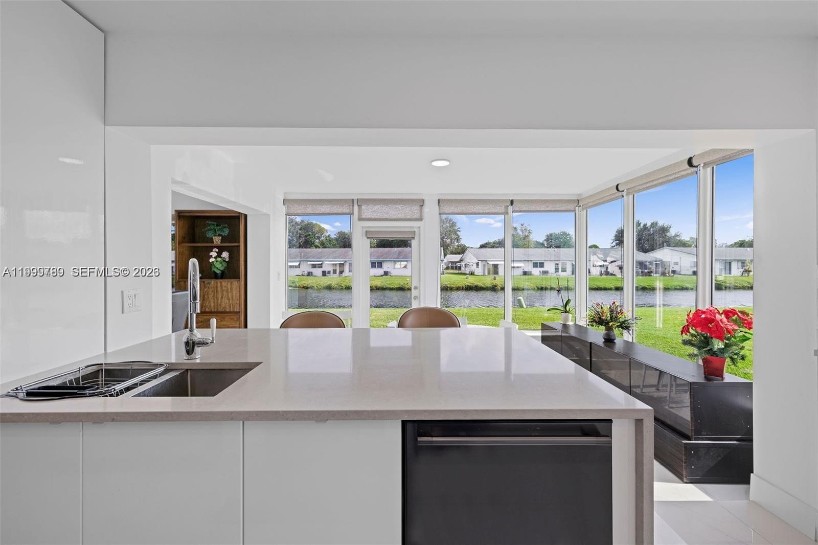 A modern kitchen island with a sink overlooks a backyard with a canal and houses — 1086 NW 88th Way, Plantation FL 33322, PLANTATION, FL