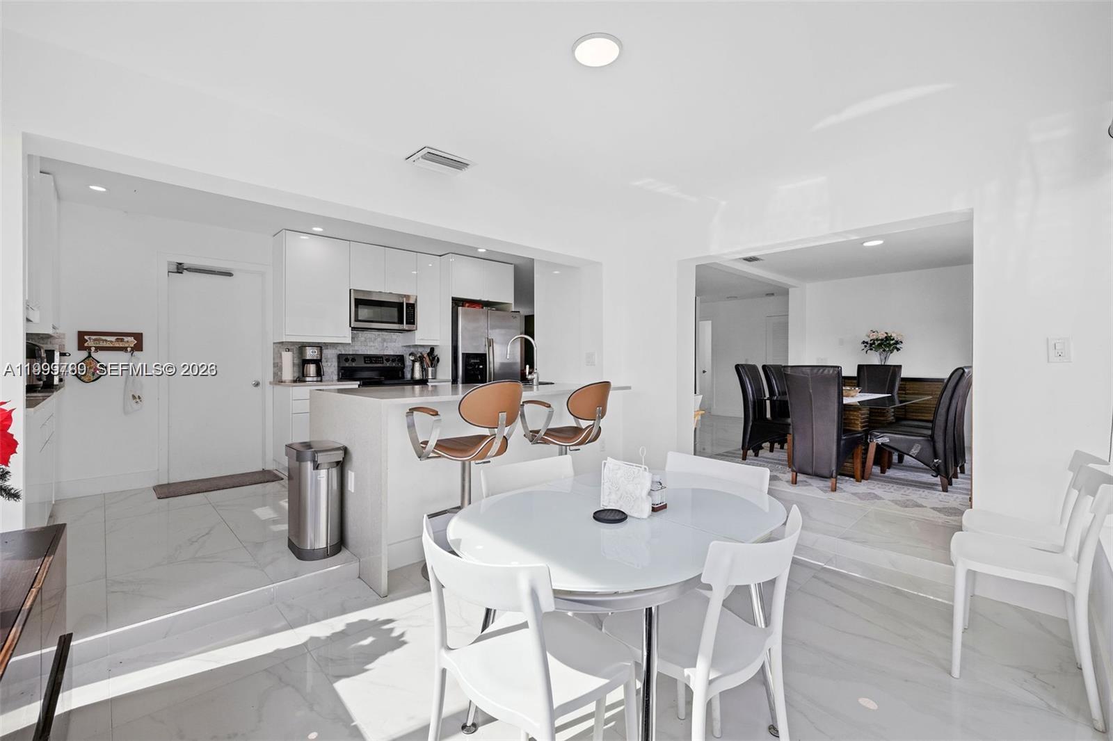 A bright, modern kitchen features white cabinetry, a breakfast bar, and an adjacent dining area — 1086 NW 88th Way, Plantation FL 33322, PLANTATION, FL