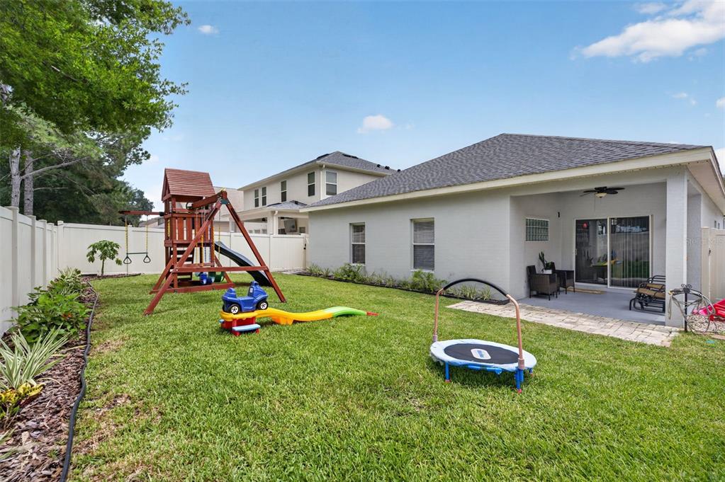 A backyard with a wooden playset, a small trampoline, and a covered patio area — 8912 VICKROY TERRACE, OVIEDO, FL