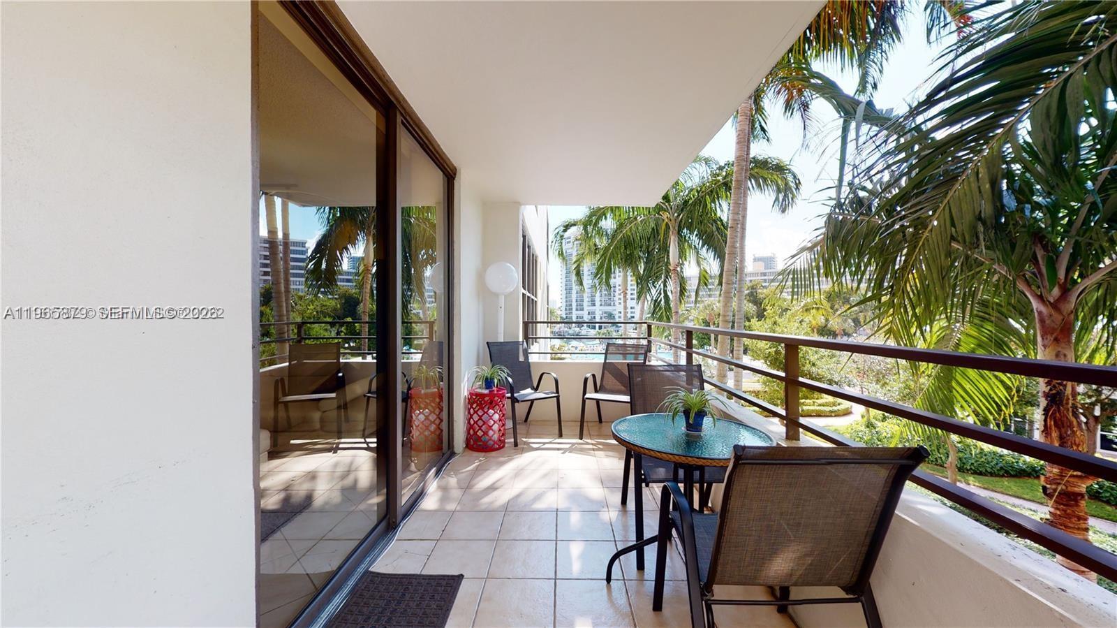 A balcony with tile flooring, patio furniture, and a view of palm trees — 2500 PARKVIEW DR # 417, Hallandale Beach FL 33009, HALLANDALE BEACH, FL