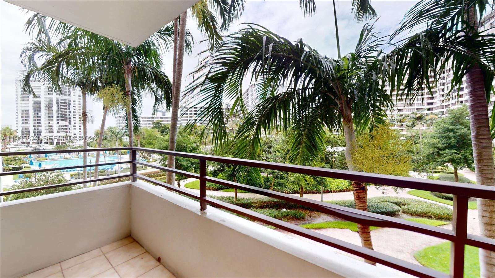 A balcony with a metal railing overlooks palm trees, a swimming pool, and apartment buildings — 2500 PARKVIEW DR # 417, Hallandale Beach FL 33009, HALLANDALE BEACH, FL