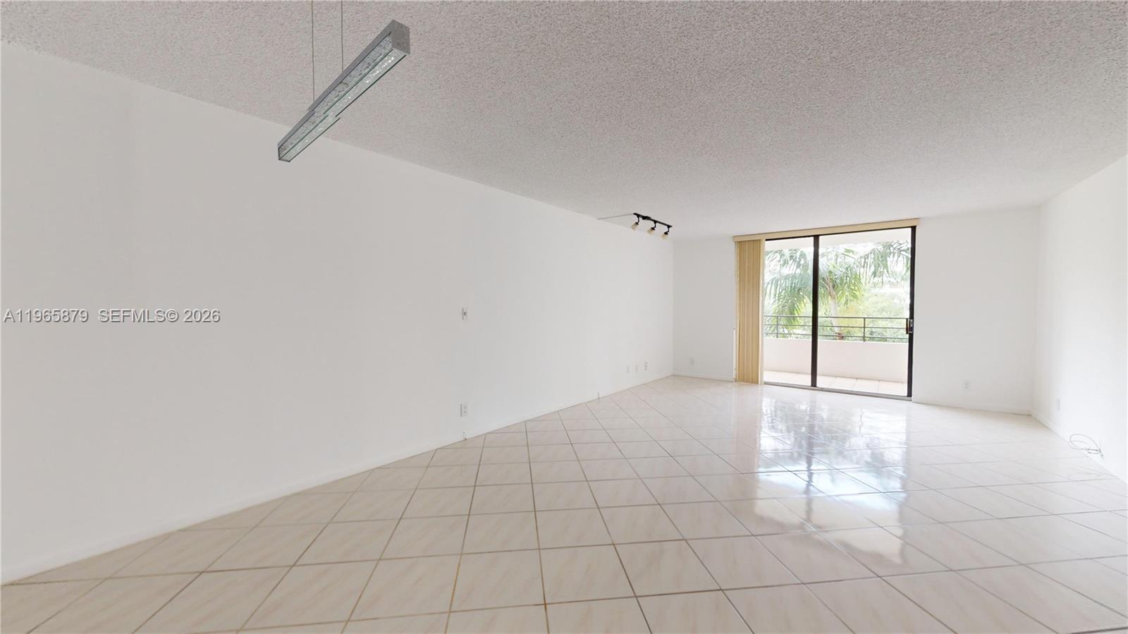 An empty living room features white walls, light-colored diagonal floor tiles, and a sliding glass door — 2500 PARKVIEW DR # 417, Hallandale Beach FL 33009, HALLANDALE BEACH, FL