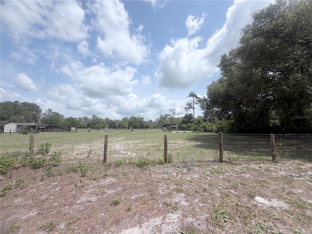 A wire fence encloses a large, grassy, sunlit field under a cloudy blue sky — TBD SW 153RD LANE, DUNNELLON, FL