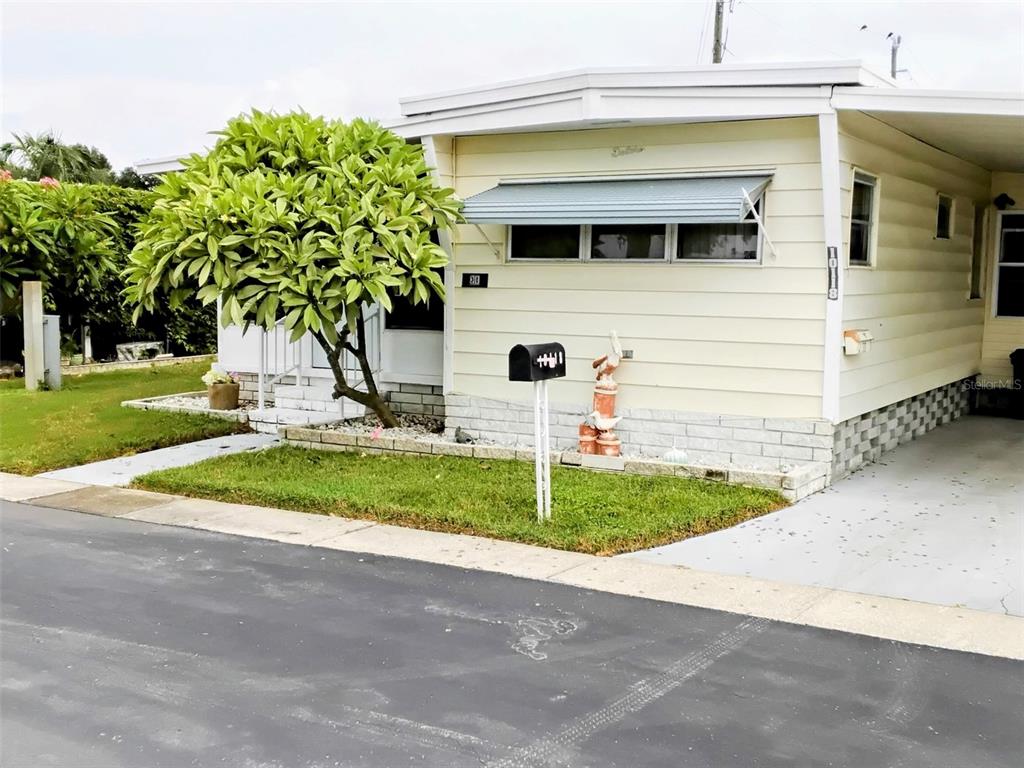 A light-colored mobile home features a small front lawn, a tree, and a mailbox — 10118 N LAKE DRIVE UNIT 30, LARGO, FL