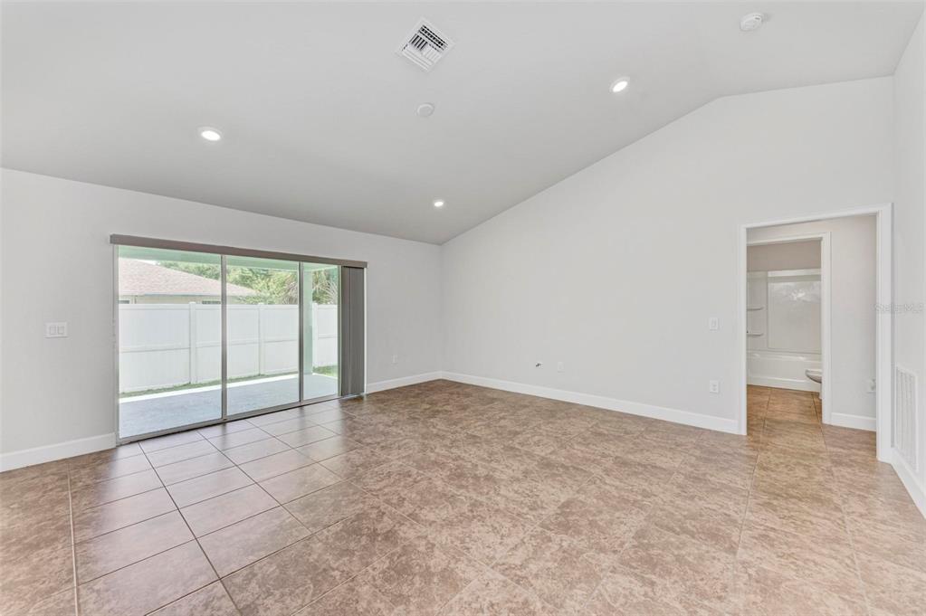 An empty room with tan tile flooring, white walls, a vaulted ceiling, and sliding glass doors — 105 DARTMOUTH ROAD, VENICE, FL