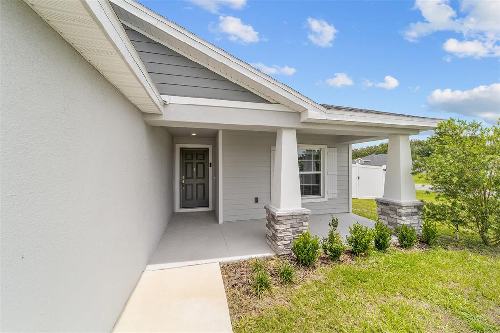 A covered front porch features stone-based columns, a gray door, and a concrete walkway — 9039 SE 44TH COURT, OCALA, FL