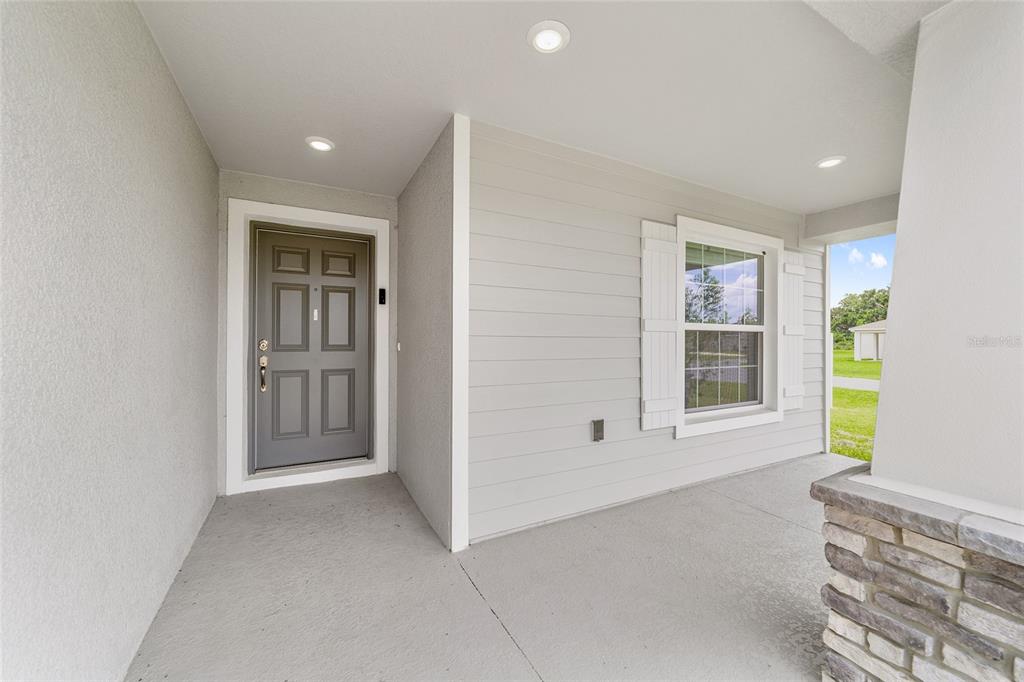 A covered front porch with a gray door, light siding, and a stone column base — 9039 SE 44TH COURT, OCALA, FL