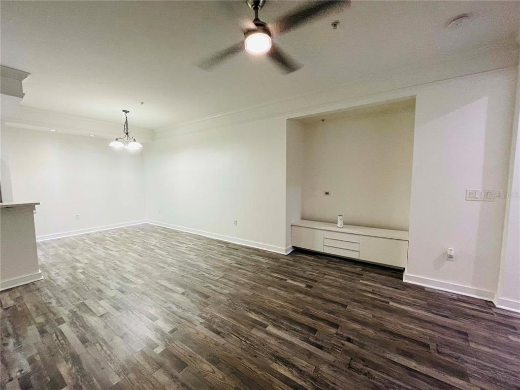 An empty living room features wood-look flooring, a ceiling fan, and a built-in media console — 12012 VILLANOVA DRIVE UNIT 103, ORLANDO, FL
