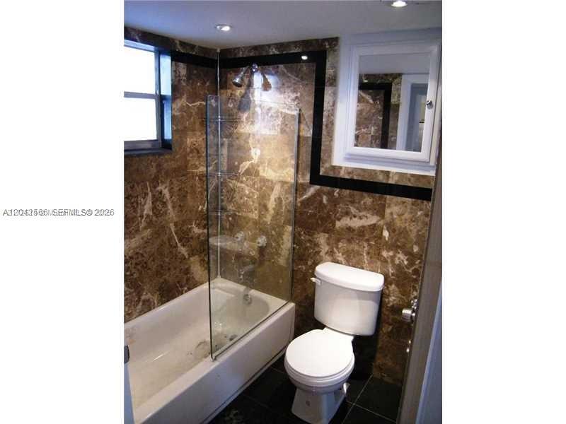 A bathroom features brown marble tile walls, a glass shower panel, and a white toilet — 701 Euclid Ave # 403, Miami Beach FL 33139, MIAMI BEACH, FL
