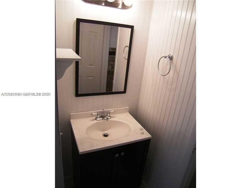 A small bathroom features a dark vanity, white countertop, rectangular mirror, and white beadboard walls — 701 Euclid Ave # 403, Miami Beach FL 33139, MIAMI BEACH, FL