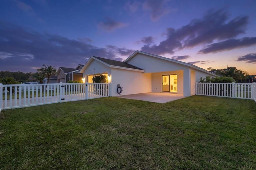 The backyard of a single-story house features a concrete patio and a white vinyl fence — 3320 MARSILI AVENUE, NEW SMYRNA BEACH, FL