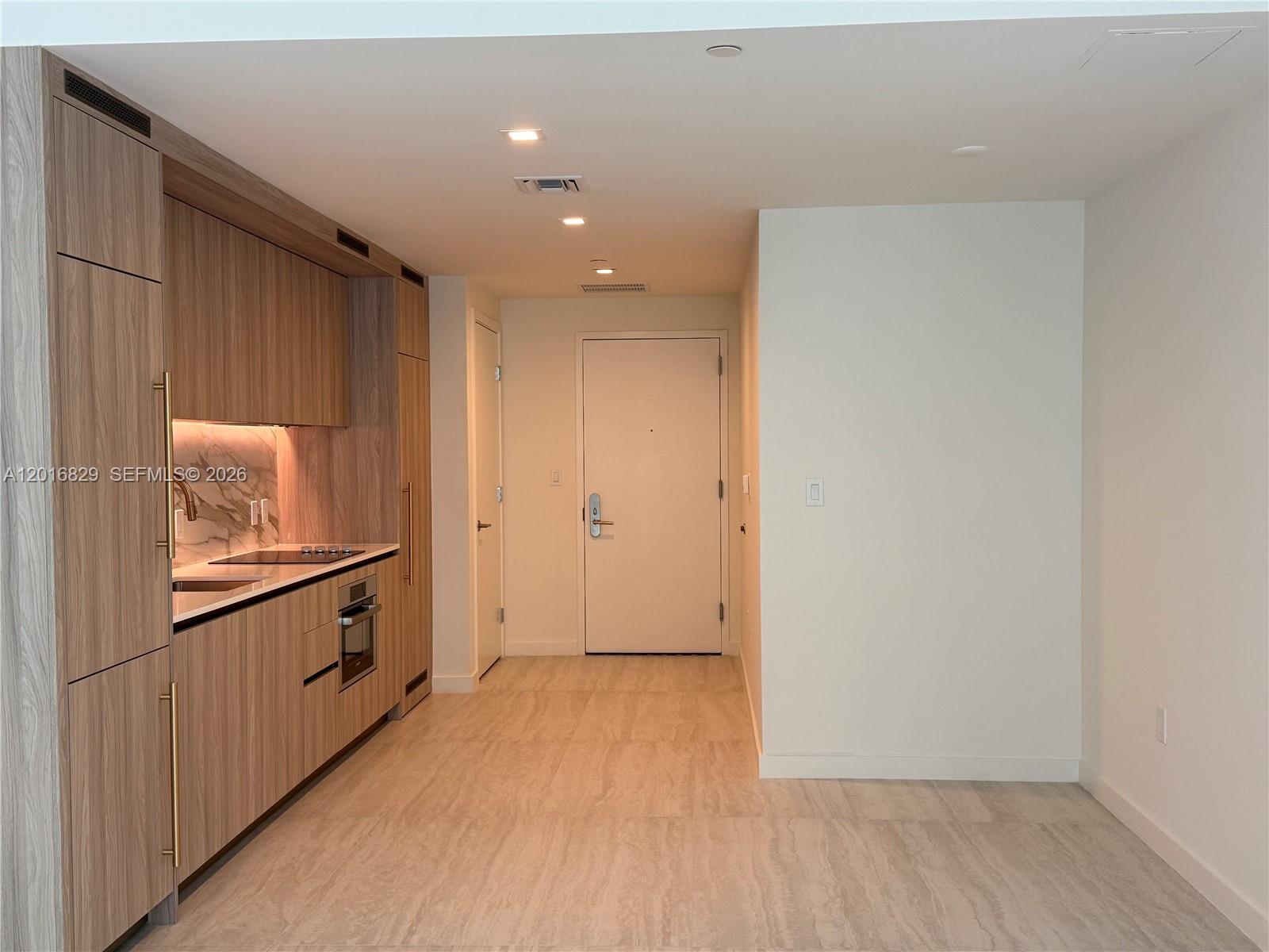 A modern kitchen features wood-grain cabinetry, marble-style backsplash, and light tile flooring — 77 SE 5TH ST # 2010, Miami FL 33131, MIAMI, FL