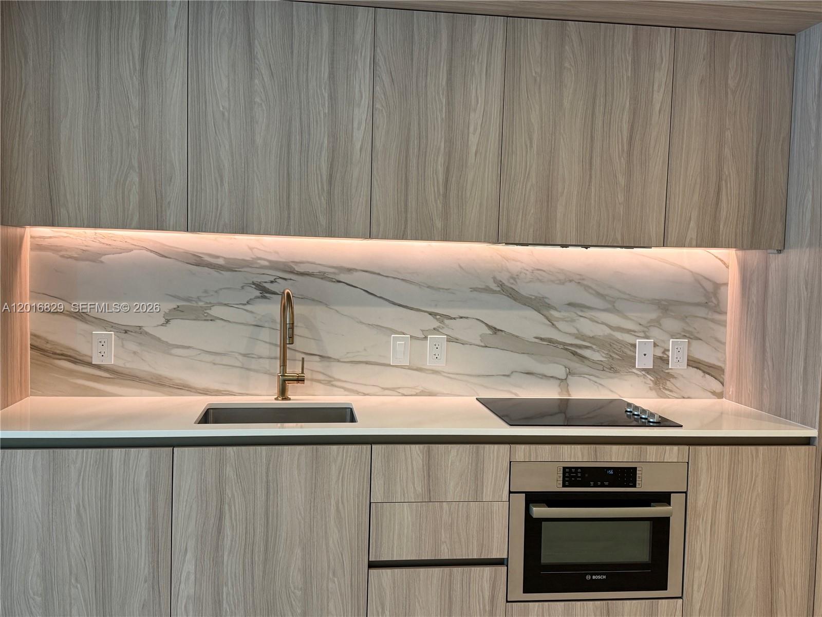 A modern kitchen features wood-grain cabinets, a marble backsplash, and a built-in Bosch oven — 77 SE 5TH ST # 2010, Miami FL 33131, MIAMI, FL