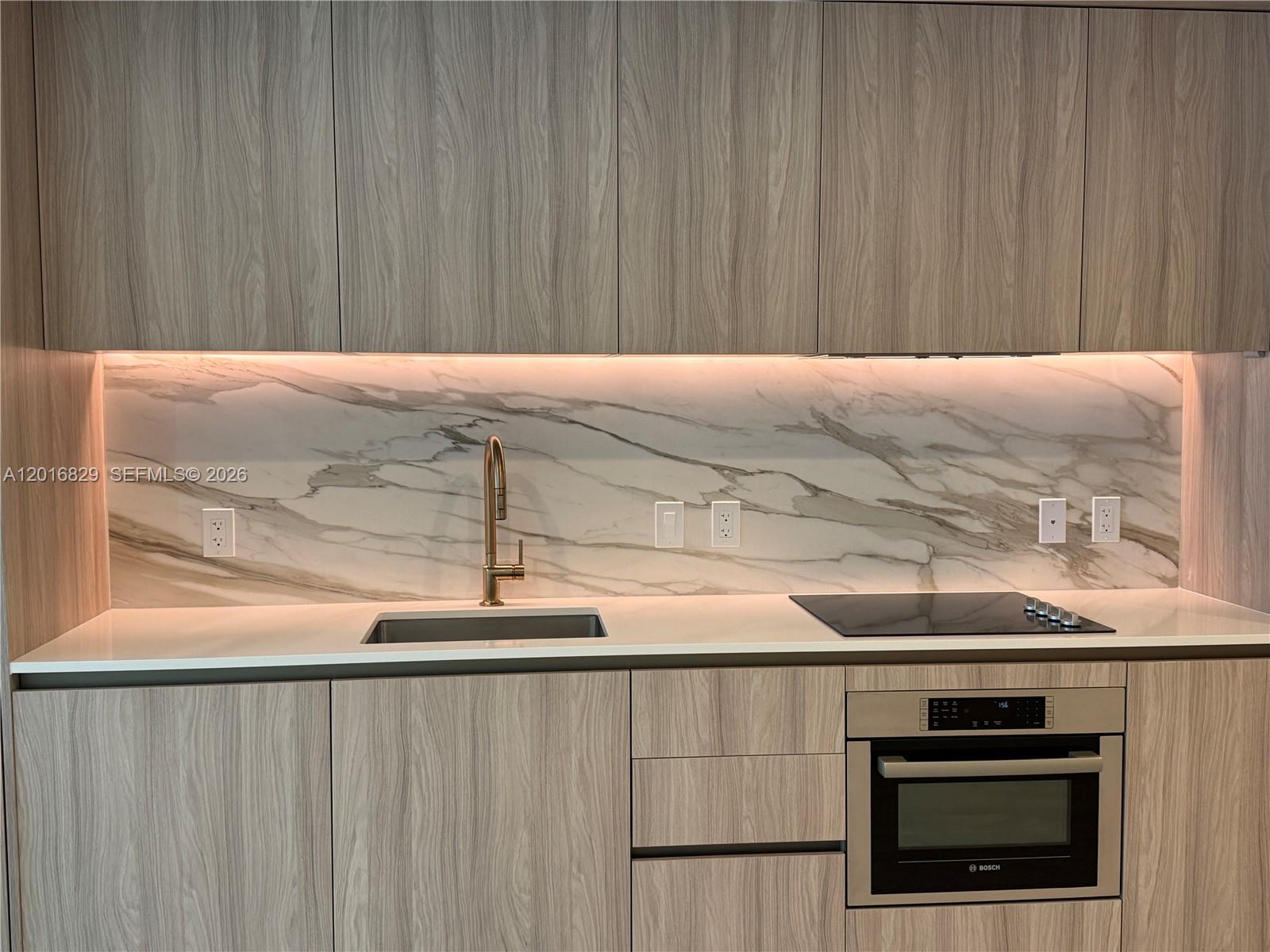 A modern kitchen features wood-grain cabinets, a marble backsplash, and a built-in Bosch oven — 77 SE 5TH ST # 2010, Miami FL 33131, MIAMI, FL