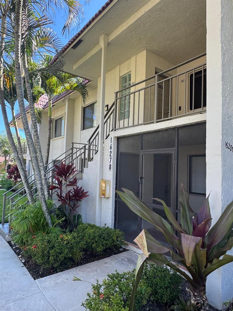 An exterior view of a two-story apartment building with a screened entryway and metal staircase — 16278 Laurel Dr # 202, Weston FL 33326, WESTON, FL
