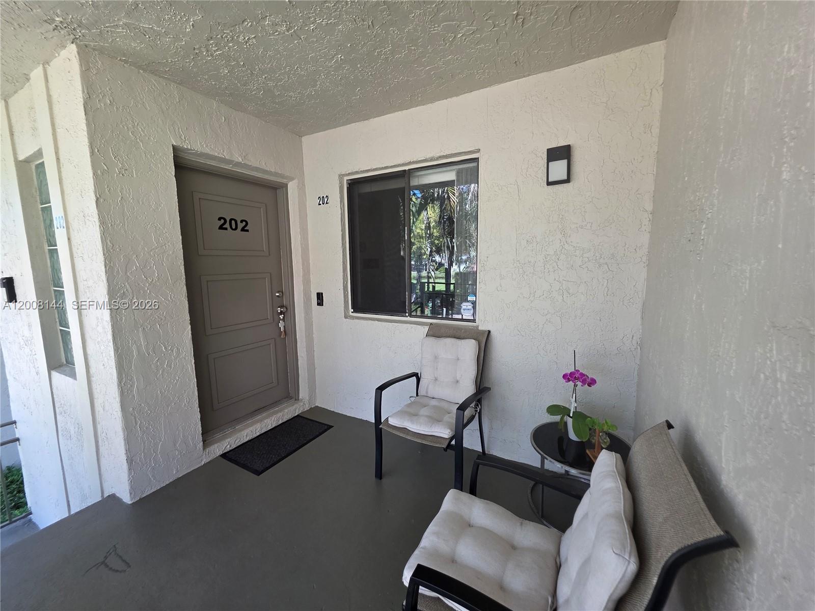A covered entryway features a gray door marked 202, a window, and two patio chairs — 16278 Laurel Dr # 202, Weston FL 33326, WESTON, FL