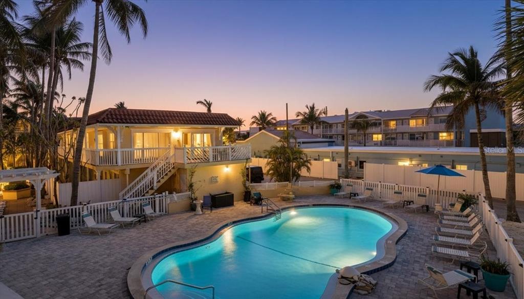An outdoor swimming pool sits in front of a two-story house with palm trees — 1325 GULF DRIVE N UNIT 125, BRADENTON BEACH, FL