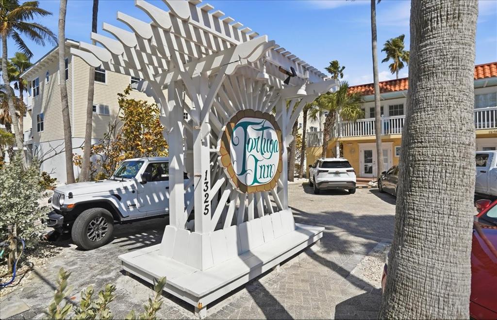 A white wooden sign for the Tortuga Inn stands in a paved parking lot — 1325 GULF DRIVE N UNIT 125, BRADENTON BEACH, FL