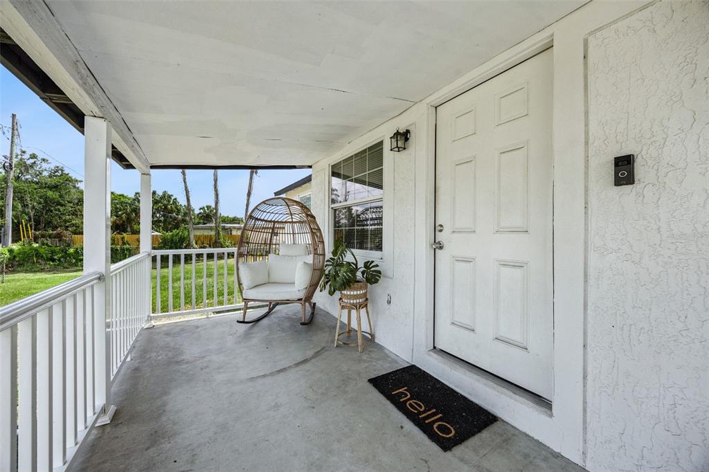 A covered front porch features a white door, a hanging egg chair, and a welcome mat — 5212 ALOHA STREET, ORLANDO, FL