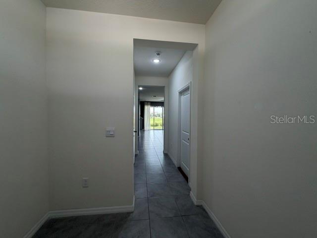 A hallway with tile flooring leads to a doorway with a view of the outdoors — 33083 FROSTED CLOVER WAY, WESLEY CHAPEL, FL