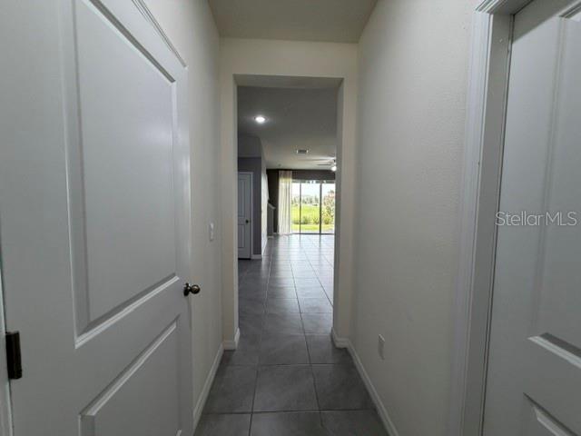 A hallway with white doors and gray tile flooring leads to an open living area — 33083 FROSTED CLOVER WAY, WESLEY CHAPEL, FL