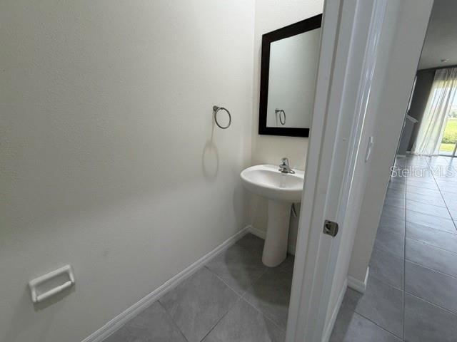 A small powder room features a pedestal sink, a wall mirror, and gray tile flooring — 33083 FROSTED CLOVER WAY, WESLEY CHAPEL, FL
