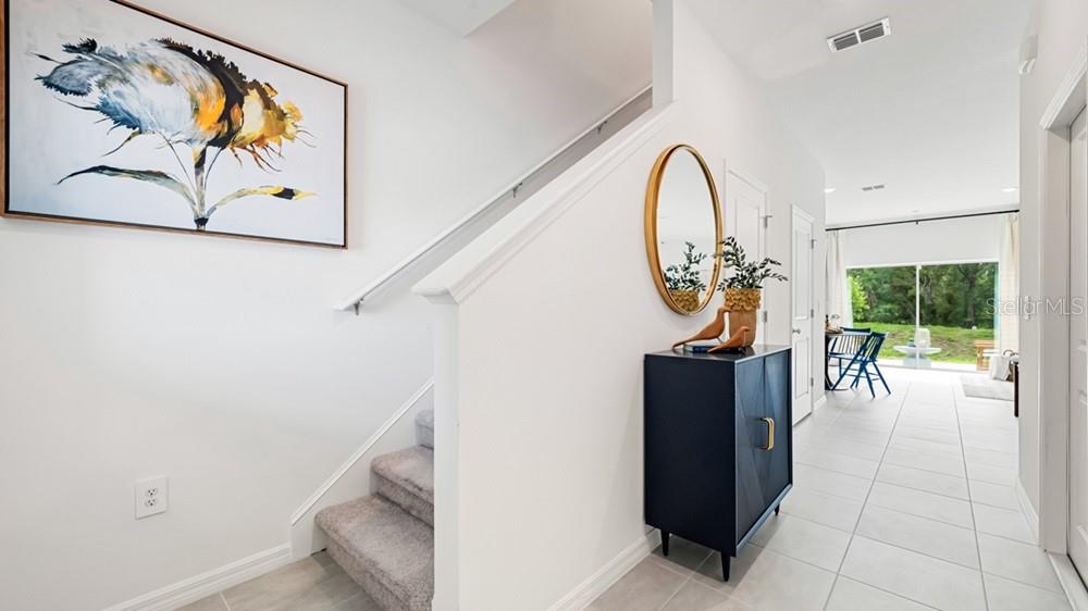 An entryway features a staircase with carpeted steps, a dark cabinet, and a round mirror — 7150 GRAND FOREST WAY, NOKOMIS, FL