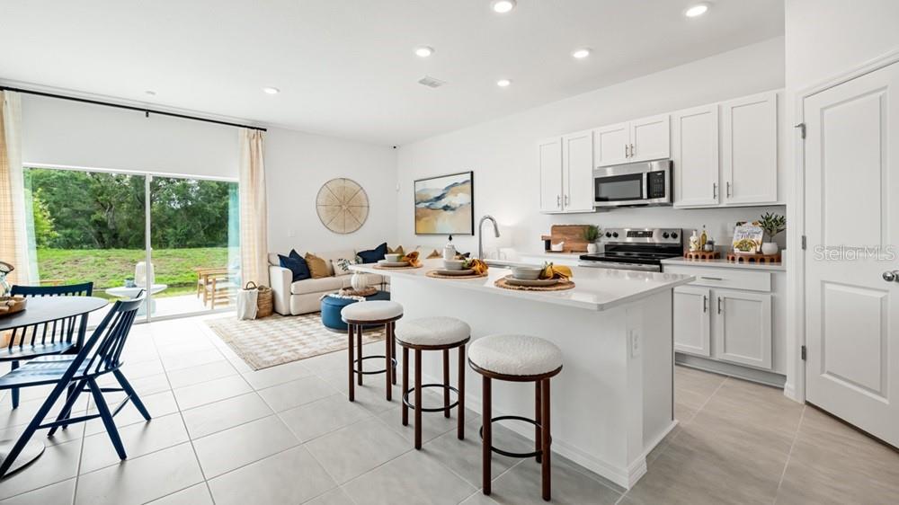 A bright open-concept kitchen and living area features white cabinetry, a central island, and tile flooring — 7150 GRAND FOREST WAY, NOKOMIS, FL