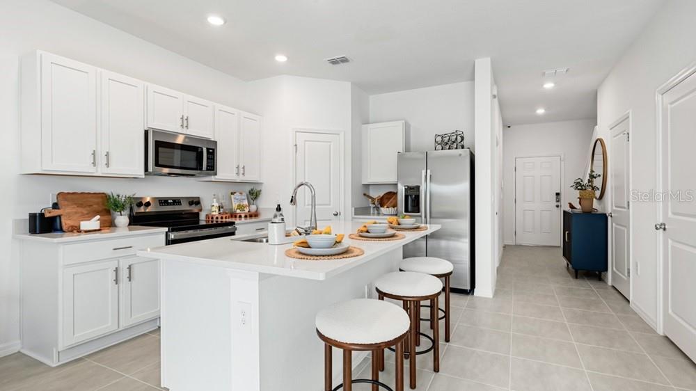 A modern kitchen features white cabinets, stainless steel appliances, a quartz island, and bar stools — 7150 GRAND FOREST WAY, NOKOMIS, FL