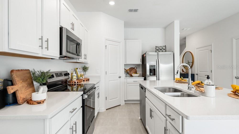 A modern white kitchen features a center island, stainless steel appliances, and quartz countertops — 7150 GRAND FOREST WAY, NOKOMIS, FL