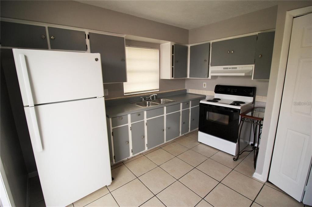 A kitchen features gray cabinets, white appliances, a double sink, and light-colored tile flooring — 9418 N 50TH STREET UNIT B, TAMPA, FL