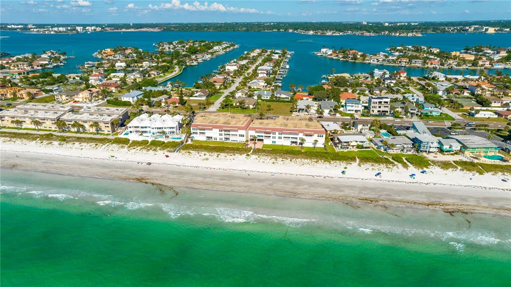 An aerial view shows beachfront apartment buildings along a sandy shore with turquoise water — 2900 GULF BOULEVARD UNIT 307, BELLEAIR BEACH, FL