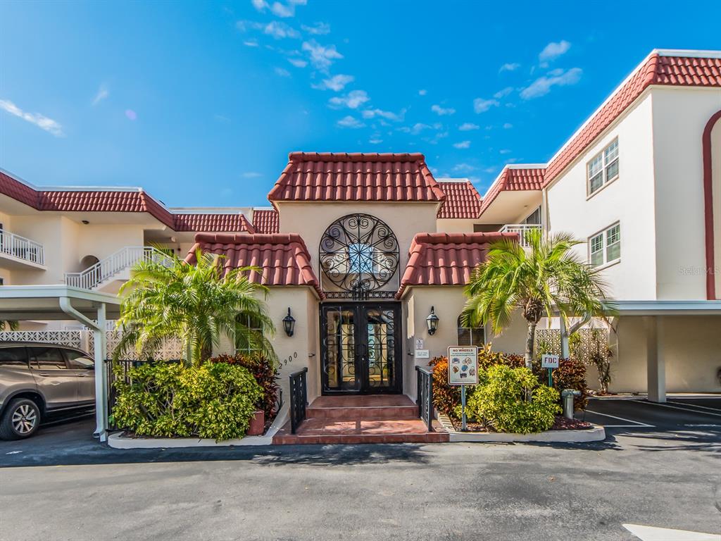 The exterior of a multi-story apartment building features a decorative arched entryway and palm trees — 2900 GULF BOULEVARD UNIT 307, BELLEAIR BEACH, FL