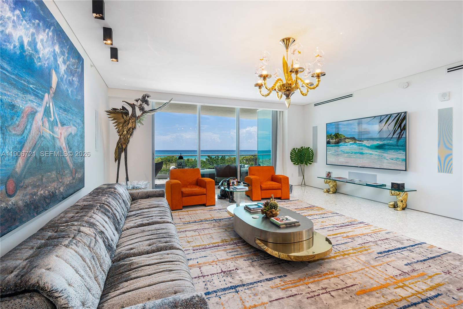 A living room features a large gray sofa, orange armchairs, a gold chandelier, and ocean views — 9349 Collins Ave # 205, Surfside FL 33154, SURFSIDE, FL