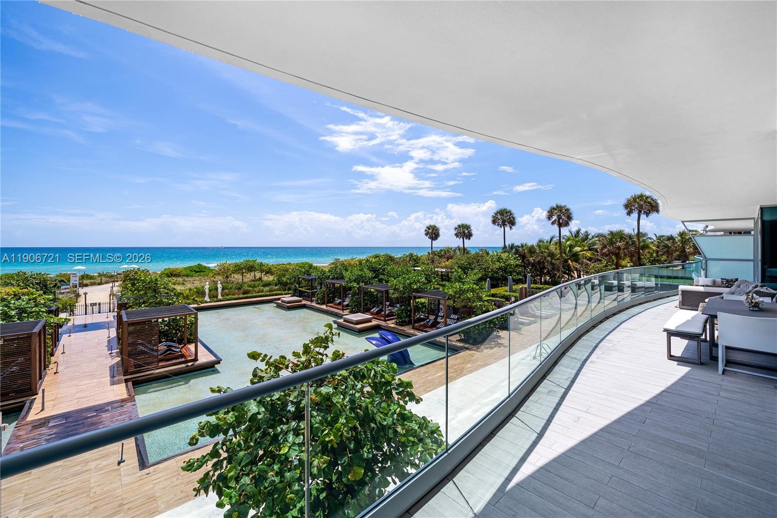 A curved balcony overlooks a swimming pool, lush landscaping, and the ocean — 9349 Collins Ave # 205, Surfside FL 33154, SURFSIDE, FL