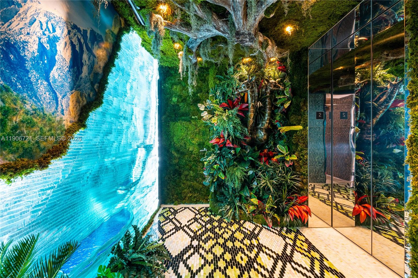 An indoor space features a glowing blue waterfall wall, a moss-covered ceiling, and mirrored elevator doors — 9349 Collins Ave # 205, Surfside FL 33154, SURFSIDE, FL