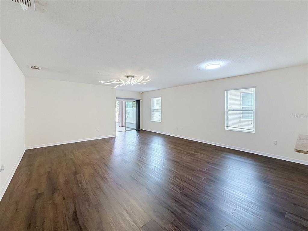 An empty living room features dark wood-look flooring, white walls, and a modern branching chandelier — 237 NOVA DRIVE, DAVENPORT, FL