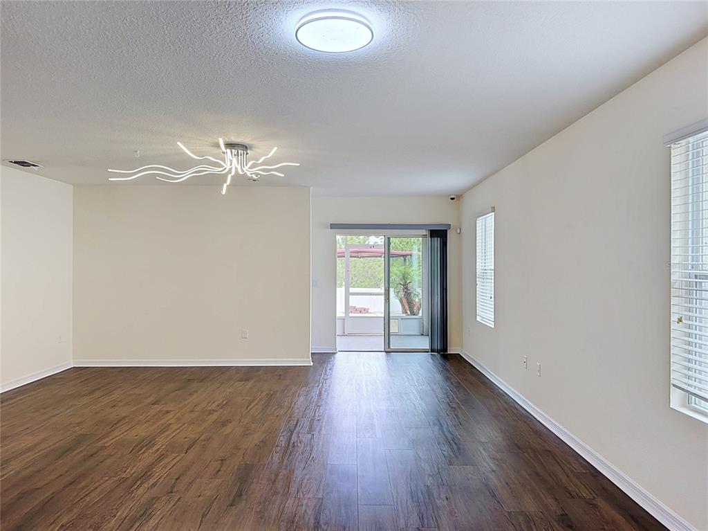 An empty living room features dark wood-look flooring, a modern light fixture, and sliding glass doors — 237 NOVA DRIVE, DAVENPORT, FL