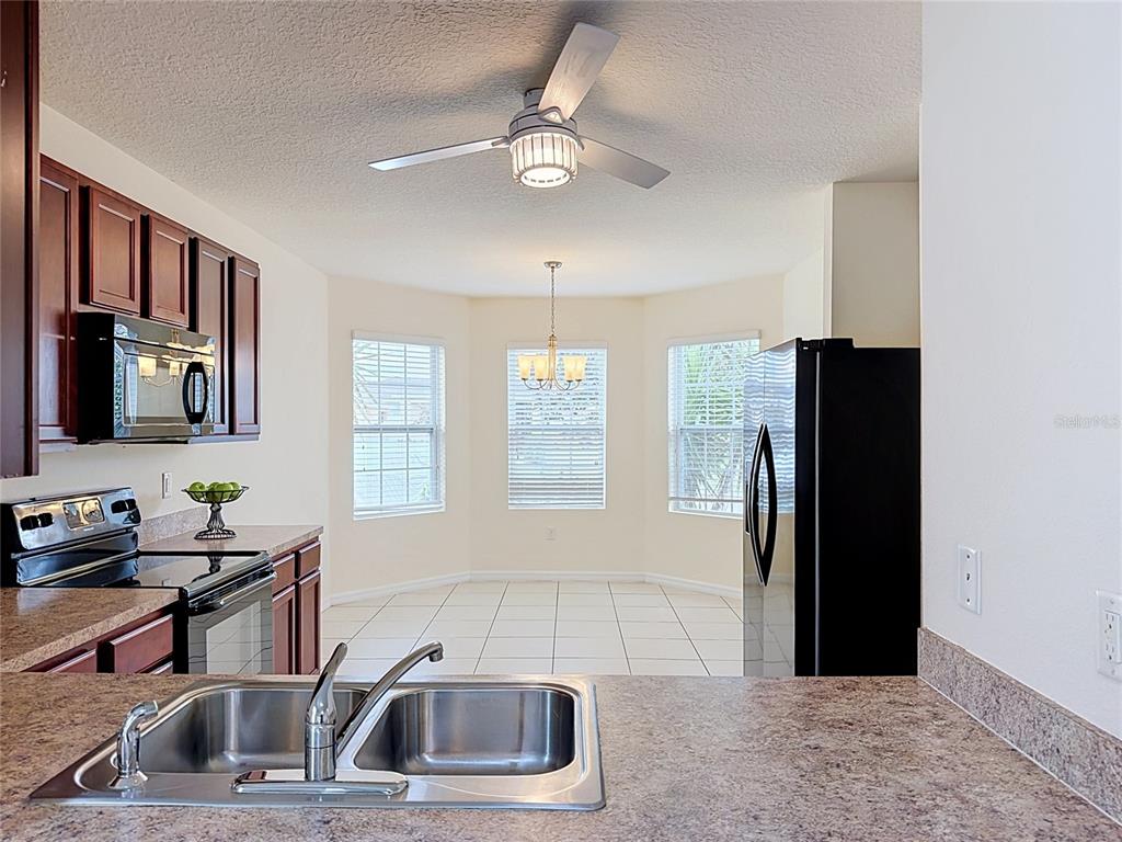 A kitchen with dark wood cabinets, granite countertops, and a stainless steel sink overlooks a dining area — 237 NOVA DRIVE, DAVENPORT, FL