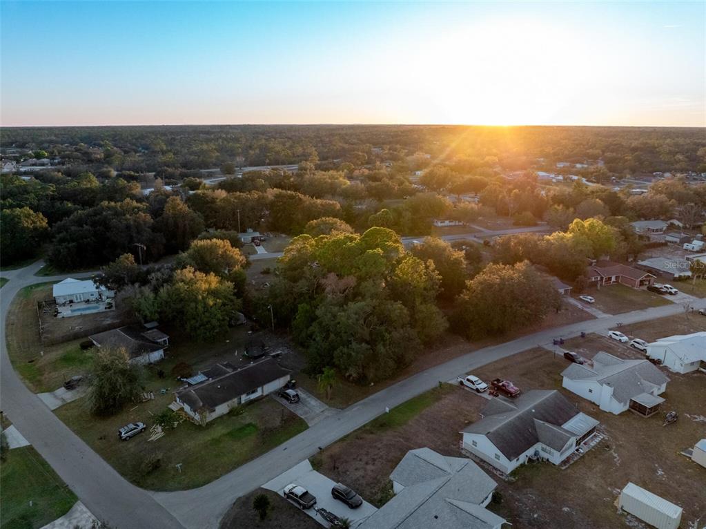 An aerial view shows a suburban neighborhood with houses, trees, and a sunset horizon — 3044 AZALEA LANE, LAKE PLACID, FL