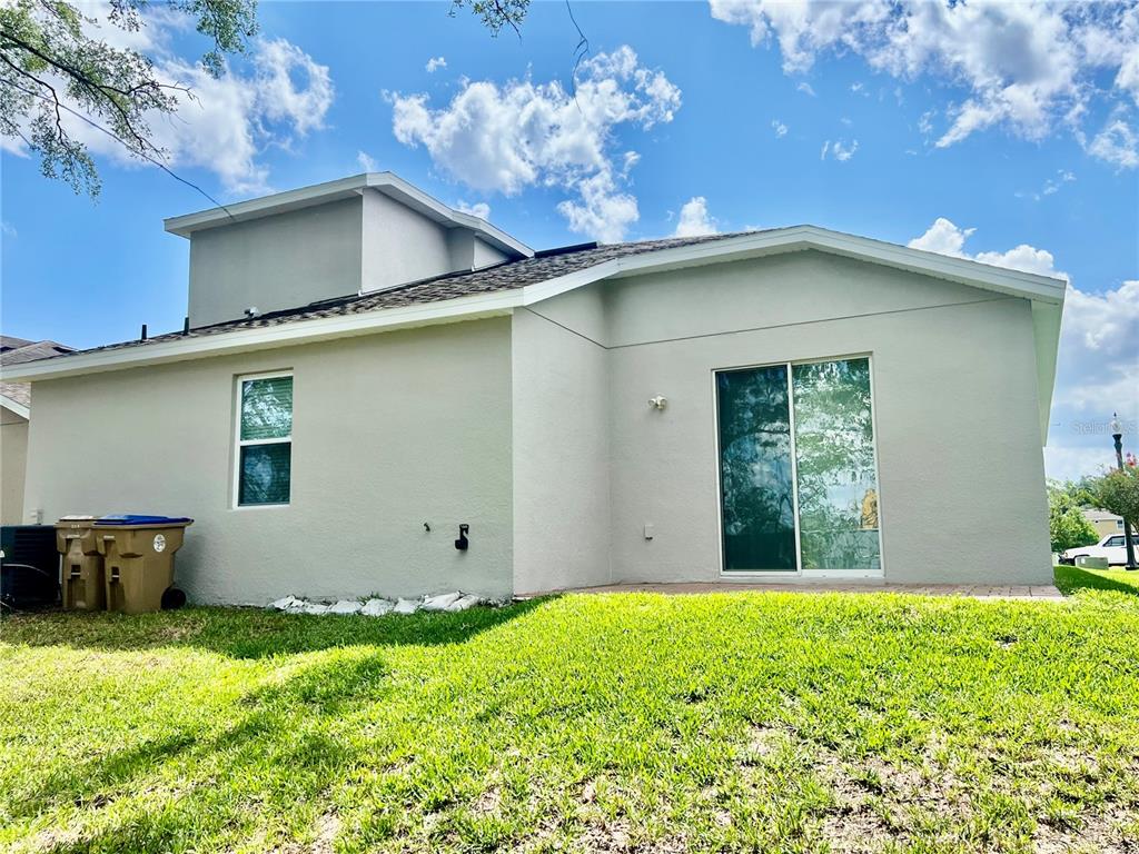 The exterior rear view of a light-colored house features a sliding glass door and window — 3215 STRATTON CIRCLE, KISSIMMEE, FL