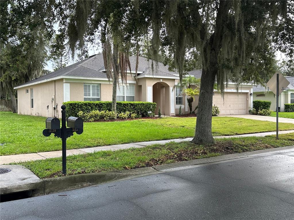A single-story beige house with a two-car garage and a large tree in the yard — 3127 CONRAD COURT, KISSIMMEE, FL
