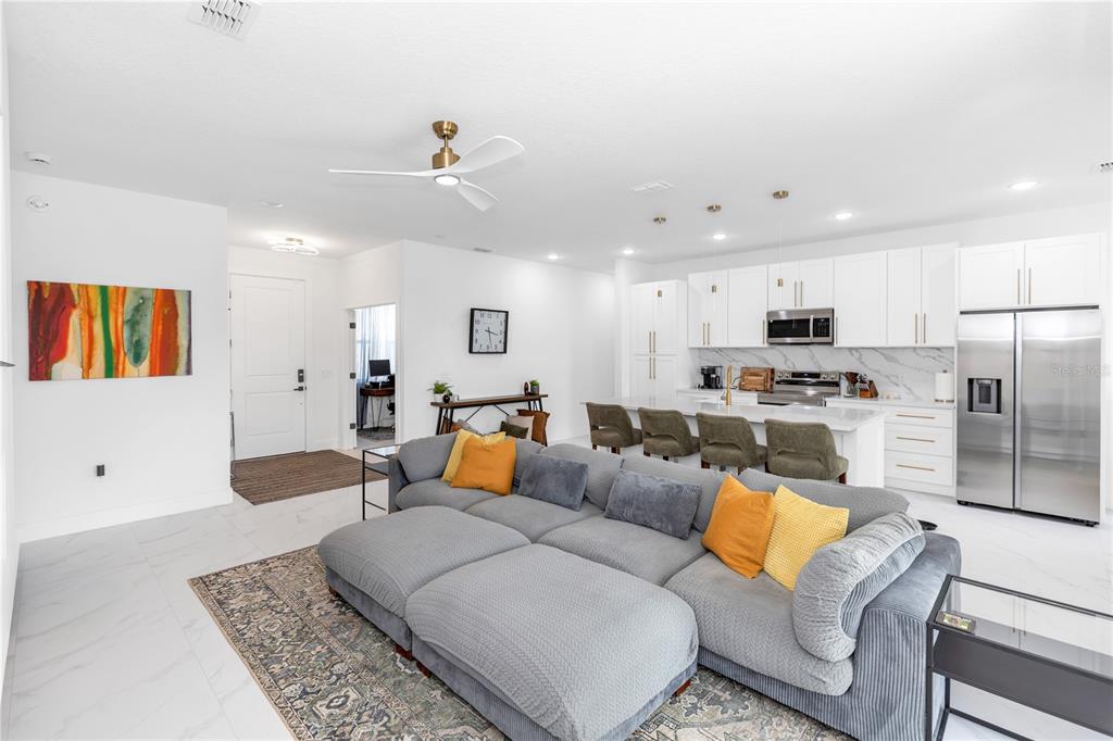 A modern open-concept living room features a large gray sectional, white kitchen cabinetry, and tile flooring — 780 KANGAROO COURT, DELTONA, FL