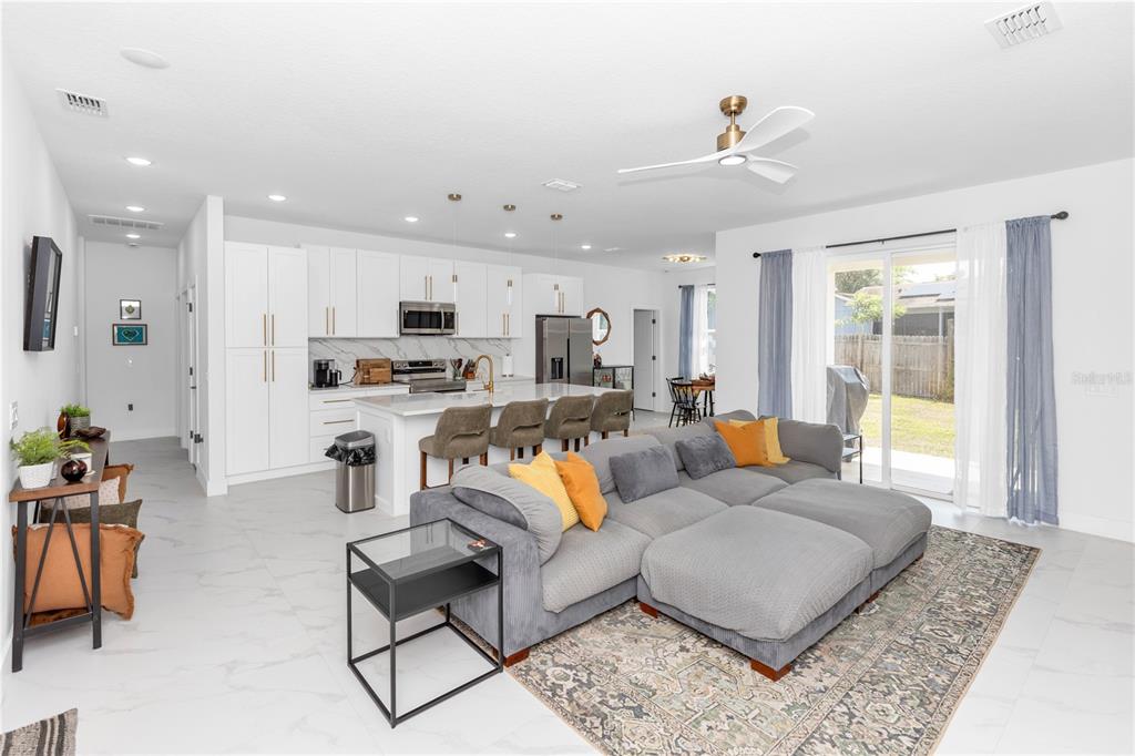An open-concept kitchen and living room featuring white cabinetry, a kitchen island, and gray furniture — 780 KANGAROO COURT, DELTONA, FL